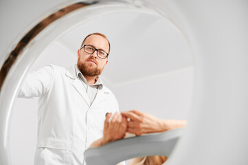 Medical computed tomography or MRI scanner. Male radiologist presses MRI button to examine female...