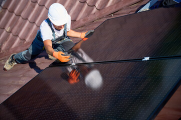 Worker building photovoltaic solar panel system on rooftop of house. Close up of man engineer in...