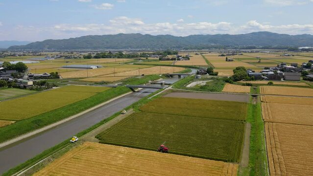 田舎の田んぼで農薬散布するトラクターの風景　上空からのパンダウン撮影