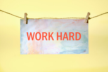 Work Hard written on paper suspended from a rope on a yellow background