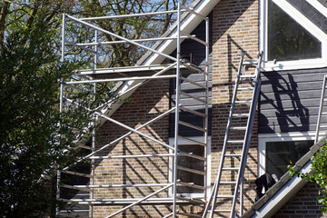 Scaffolding and ladders at a house that is being painted. Sunny, bamboo, trees, sky. spring, May,...