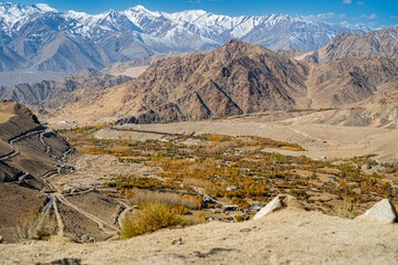 Spectacular high roads wind through rugged mountains beneath blue skies and the remote snow-capped peaks of Ladakh, India.