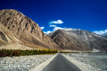 Spectacular high roads wind through rugged mountains beneath blue skies and the remote snow-capped...