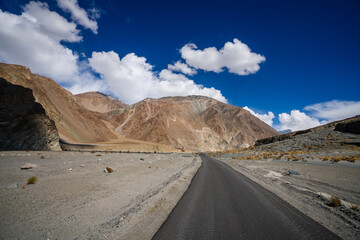 Spectacular high roads wind through rugged mountains beneath blue skies and the remote snow-capped peaks of Ladakh, India.