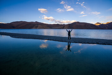 A person standing with arms raised at a serene mountain lake during sunset, reflecting the joy of nature.