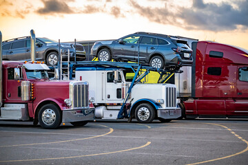 Classic bonnet big rig semi-trucks with loaded semi trailer take a break and standing on the truck stop parking lot at evening time
