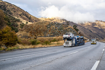 Classic car hauler big rig semi truck transporting cars on the semi trailer climbing uphill on the...