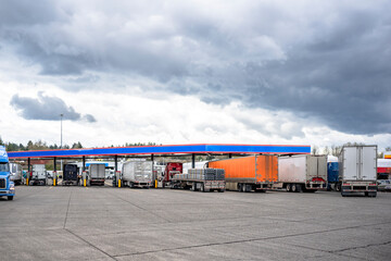 Different industrial big rigs semi trucks with loaded semi trailers filling up tanks at a gas station on the truck stop