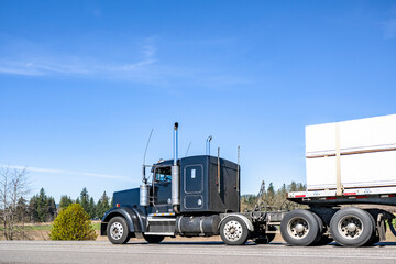 Extended cab black classic big rig semi truck transporting cargo on flat bed semi truck driving on the flat h road