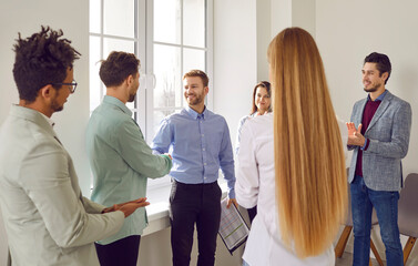 Group of young business people standing in circle in office finishing meeting. Two men shaking...