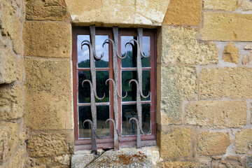 Medieval mullioned window with an ornate wrought iron security grill.
