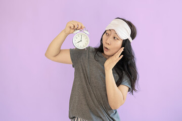 Young shocked Asian woman wrapped wears jam sleep eye mask rest relax at home hold in hand alarm clock isolated on pastel pink background studio. Good mood night nap concept