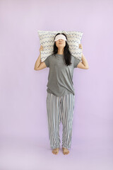 Full body smiling happy young Asian woman wears pyjamas jam sleep eye mask rest relax at home hold pillow isolated on plain pastel pink background. Good mood night nap concept