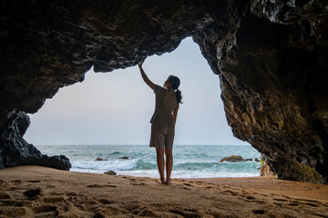 The back view of a woman standing in a cave by the sea.