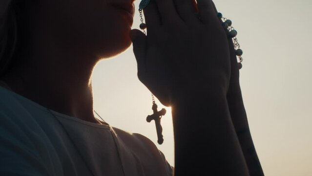 Woman praying while sun shinning through rosary beads