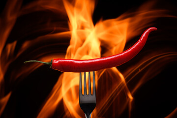 red chili pepper, pricked on a fork, on a background of burning fire, flames on a black background