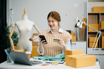 Young woman running online store Startup small business SME, using smartphone or tablet taking...