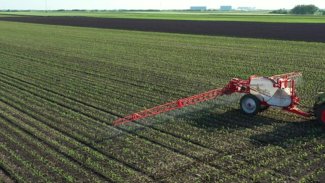 Above view, dolly move around tractor until spraying farmland, dragging mounted wide agricultural sprayer on a field with young new cereal crop, corn, maize.