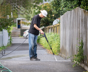 Man cleaning concrete driveway using a water blaster.