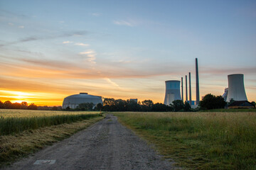 The morning in a wheat field in the background a coal-fired power station at sunrise. Landscape shot of nature and industry at the Staudinger power plant, Hainburg, Bavaria, Germany