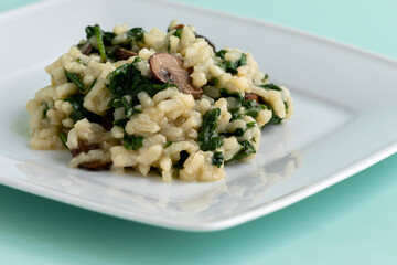 Homemade vegan spinach and portobello mushroom risotto on a white rectangular plate. Healthy vegan eating concpt.