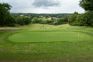Campo de golfe rodeado por verdes campos a alguma floresta à volta com um golfista ao fundo a...