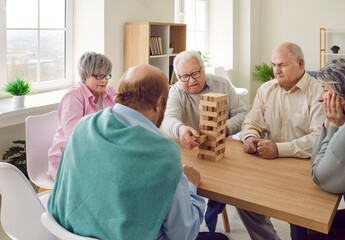 Group of elderly people playing board games in senior care centre or retirement home. Several old...