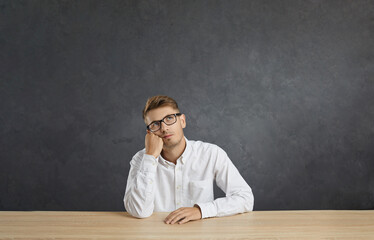 Portrait of young pensive male employee sitting at table and bored, tired and need relax day....