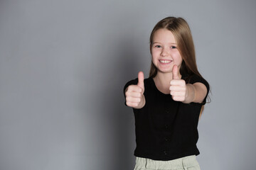 A girl gives two thumbs up with a beaming smile, a gesture of approval. Captures the positivity and...
