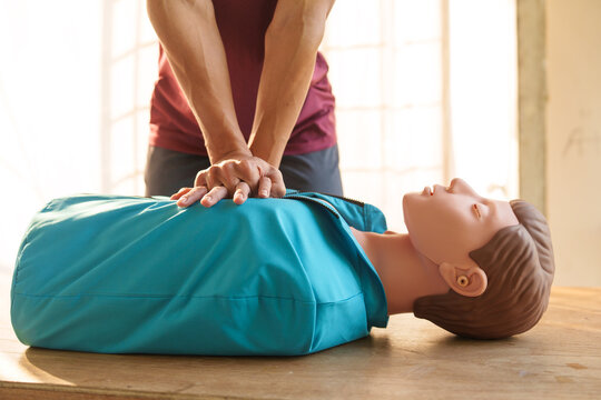 Close-up of middle-aged Asian male hands performing cardiopulmonary resuscitation (CPR) on a training dummy. Vital techniques include defibrillation, chest compressions, and maintaining the airway.