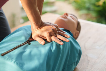 Close-up of middle-aged Asian male hands performing cardiopulmonary resuscitation (CPR) on a training dummy. Vital techniques include defibrillation, chest compressions, and maintaining the airway.