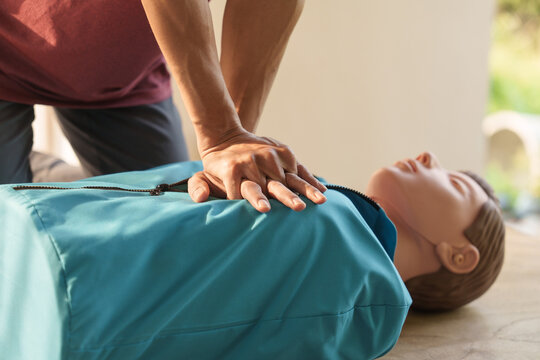 Close-up of middle-aged Asian male hands performing cardiopulmonary resuscitation (CPR) on a training dummy. Vital techniques include defibrillation, chest compressions, and maintaining the airway.