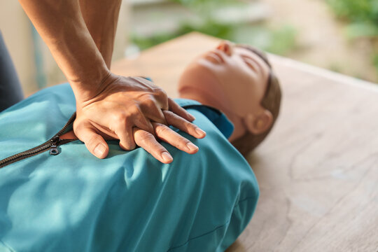 Close-up of middle-aged Asian male hands performing cardiopulmonary resuscitation (CPR) on a training dummy. Vital techniques include defibrillation, chest compressions, and maintaining the airway.