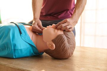 Close-up of middle-aged Asian male hands performing cardiopulmonary resuscitation (CPR) on a training dummy. Vital techniques include defibrillation, chest compressions, and maintaining the airway.