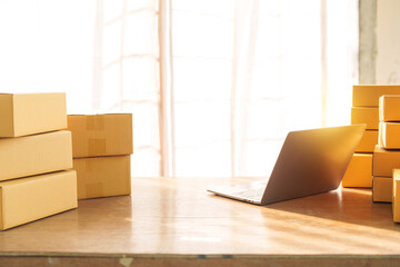 Parcel sme boxes on shelf alongside colorful shopping bags near a laptop on a table. SMEs thriving in online shopping operate from home offices, making packaging a central aspect of their business.