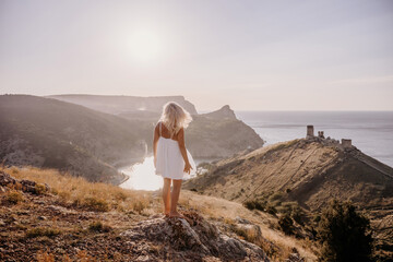 A woman stands on a hill overlooking a body of water. The sky is clear and the sun is shining...