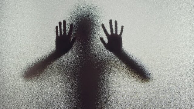 A young woman's silhouette behind the frosted window touches the glass