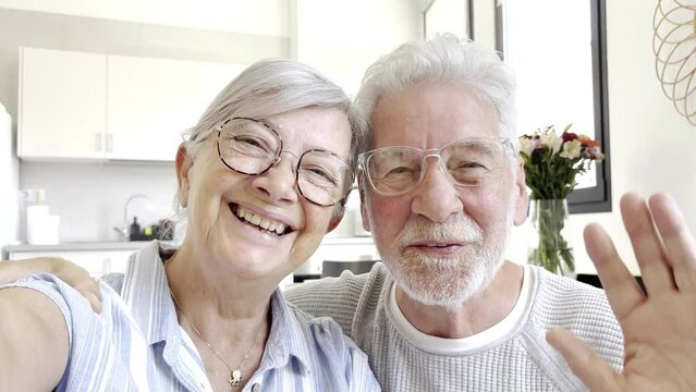 Sixty years couple, elderly parents communicates with grown up children using modern technologies makes video call, wave hands gesture of hello or goodbye sign, older generation and internet concept
