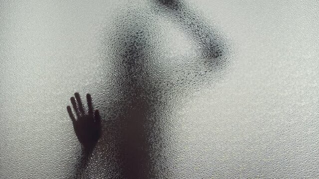 A female silhouette behind the frosted window dances slowly 