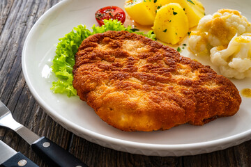 Crispy breaded fried pork chop, boiled potatoes and cooked cauliflower on wooden table
