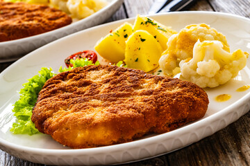 Crispy breaded fried pork chop, boiled potatoes and cooked cauliflower on wooden table
