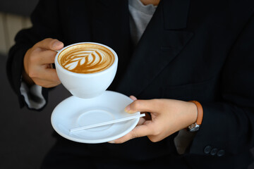 Close up shot of young woman holding a cup of coffee with latte art
