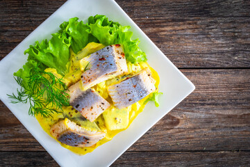 Marinated herring fillets in mustard sauce with dill and lettuce on wooden table
