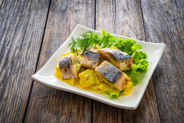 Marinated herring fillets in mustard sauce with dill and lettuce on wooden table
