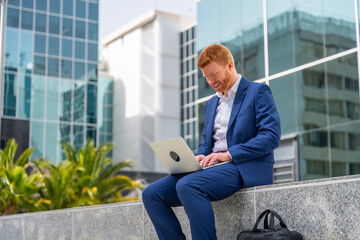 Businessman using laptop sitting outside an office block