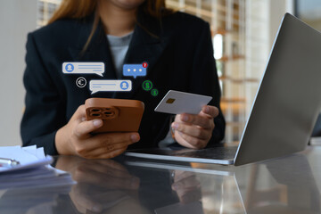 Young female worker holding credit card and using mobile phone for financial transaction