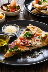 Roman Pinsa slice with mozzarella cheese, ripening ham and mushrooms on wooden table
