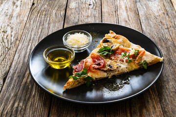 Roman Pinsa slice with mozzarella cheese, ripening ham and mushrooms on wooden table
