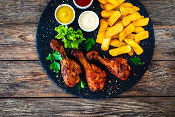 Roast chicken drumsticks and French fries on wooden table
