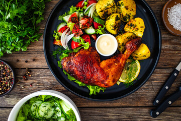 Oven roasted chicken thigh with boiled potatoes and fresh vegetables on wooden table
